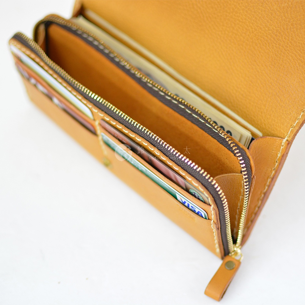 職人手作皮革長夾，展示內部結構，包含多個卡槽與鈔票夾層，整體以淺棕色皮革製成，搭配金色拉鍊與同色系皮革拉環。