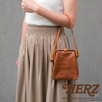 職人手作皮革Organ迷你杜勒斯側背包，採用柔軟的棕色皮革製成，包身呈現復古的口金設計，搭配細長皮革背帶，由女性模特兒斜背展示。