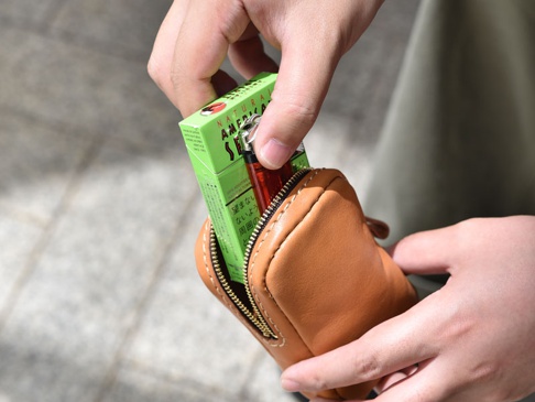 職人手作咖啡色皮革菸盒收納包，拉鍊開口，內含一盒綠色香菸及打火機。