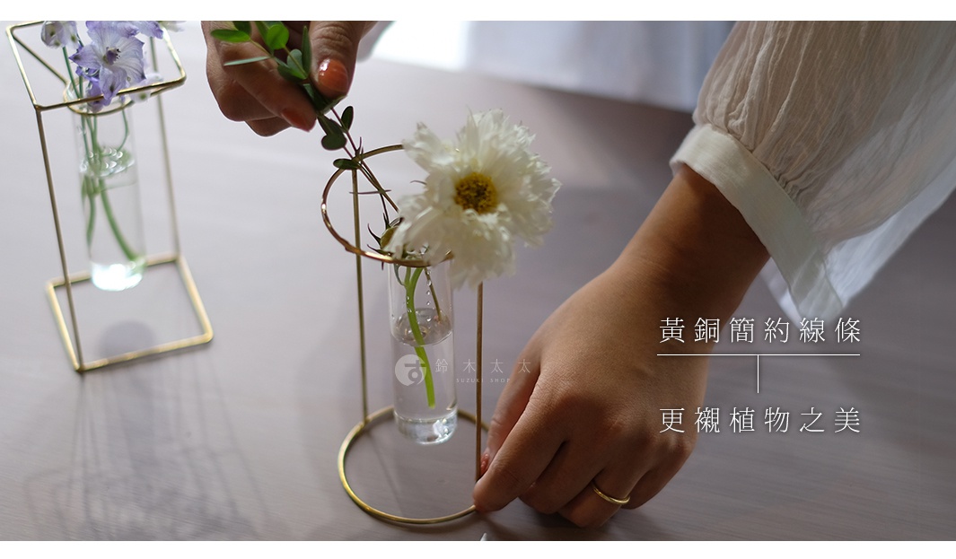 黃銅製成的簡約線條花器，支撐著透明玻璃試管，內有清水和一株白色花朵，及另一款花器內有紫色花朵。