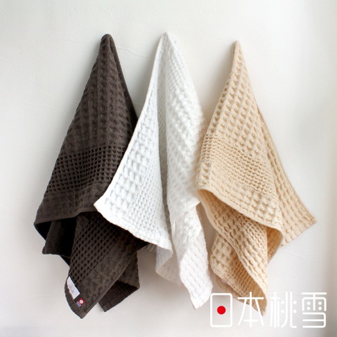 今治鬆餅毛巾，共三色，深棕色、白色、米白色，皆為格紋織法，懸掛於白色牆面。