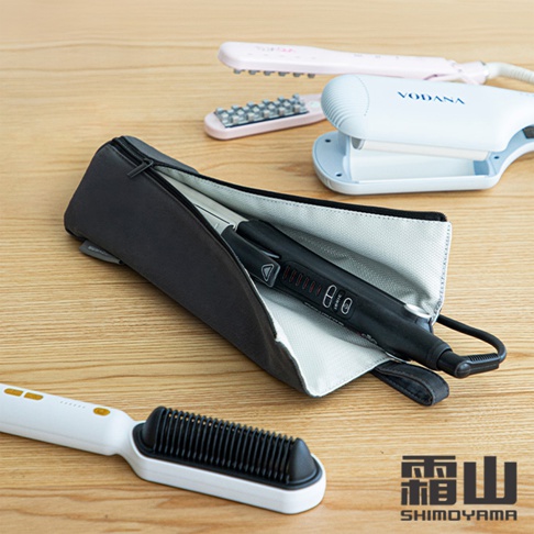 一個黑色拉鍊式隔熱收納袋，內部襯有淺灰色材質，收納了一支黑色電棒燙。袋子旁邊有一支白色電熱梳，背景還有粉色和白色的電棒燙。