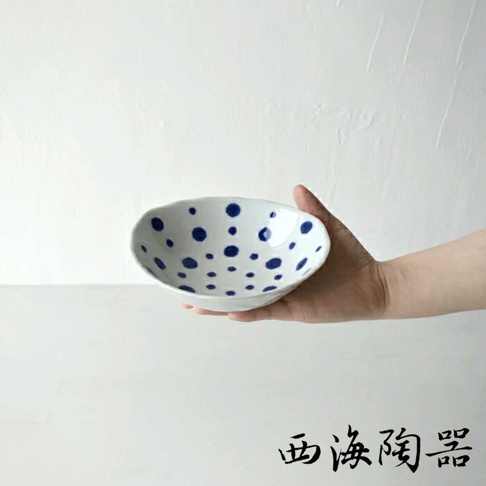 一只手托著一個白色陶瓷深盤，盤內佈滿藍色圓點圖案。
