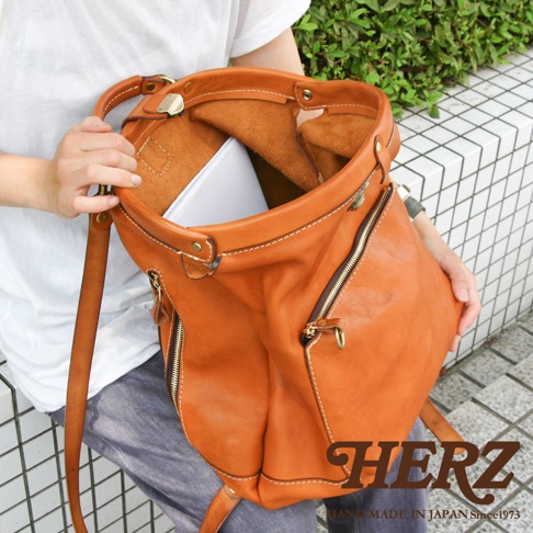 職人手作皮革後背包，採用棕褐色皮革，設有雙拉鍊前袋，內襯為淺棕色皮革，展示了其獨特的手工質感與設計。