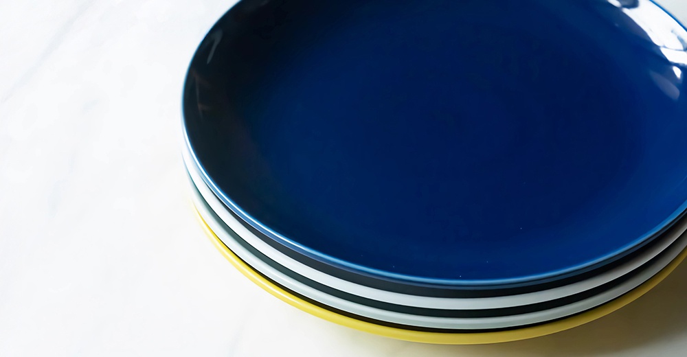 堆疊的波佐見燒陶瓷料理盤，由深藍、白色、灰色和黃色組成，呈現簡約設計。