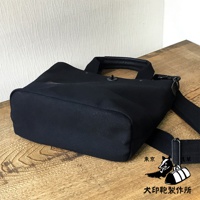 黑色帆布製成的兩用托特包，帶有皮革提把和可拆卸肩帶。包身結構紮實，底部為方形，材質為耐磨帆布。