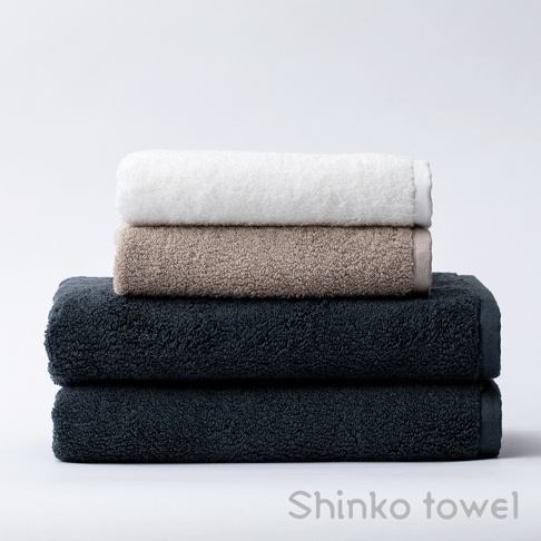 堆疊的泉州匹馬棉浴巾，由上至下分別為白色、淺褐色和深藍色，質地柔軟。