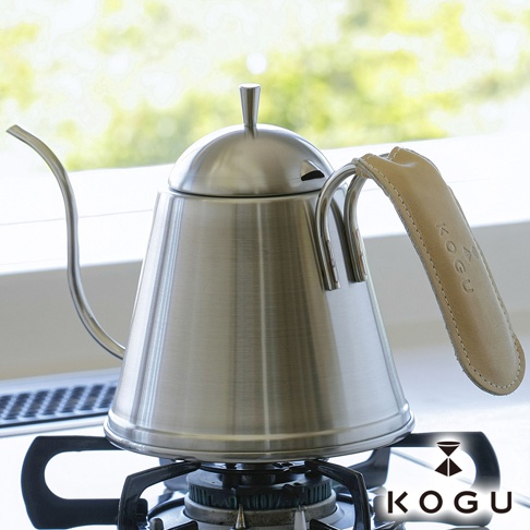 銀色金屬咖啡手沖壺，配備米色植鞣皮革隔熱套，皮革上壓印著「KOGU」品牌字樣。