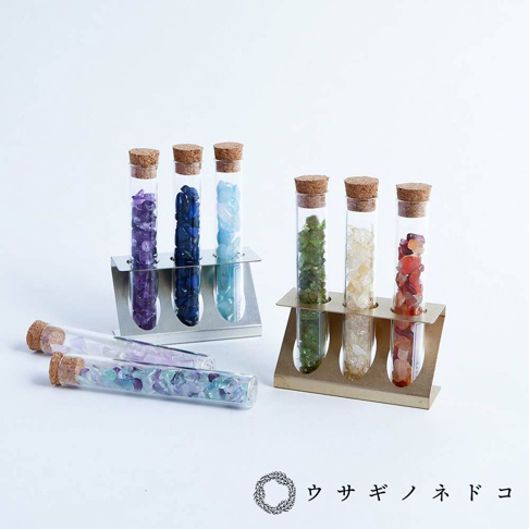 銀色金屬和金色金屬試管瓶放置架，各裝有帶軟木塞的玻璃試管，試管內填充有紫色、藍色、綠色、黃色、紅色等不同顏色的小碎石。