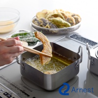 銀色不鏽鋼方型炸物鍋，鍋內裝有熱油，一塊裹粉的南瓜片正被木筷夾起準備油炸。背景有濾油網盛裝炸好的天婦羅，以及裝有麵糊的玻璃碗。