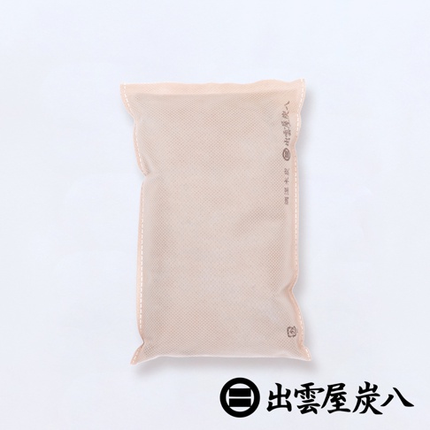 淺褐色布質包裝的寬版調濕木炭，表面有細小的網狀紋路，側邊縫線清晰，印有品牌標誌與文字，整體為長方形的居家收納用品。