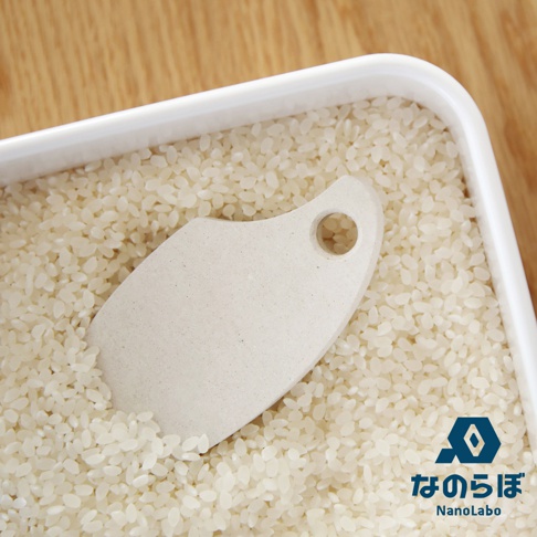 白色珪藻土製成的米之守護神防潮塊，形狀類似葉片，帶有圓形掛孔，置於裝滿米粒的白色容器中。