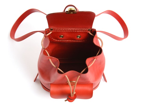 紅色皮革迷你後背包，頂部翻蓋敞開，露出內部空間，兩側有抽繩設計，正面有一個小隔層，配有皮革束帶和金屬扣。