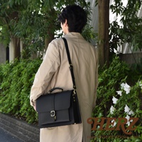 職人手作黑色皮革三用單扣商務後背包，展示於一位身穿米色外套的男士肩上，配有可調節的黑色皮革肩帶和金色扣環。