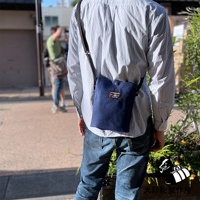 深藍色燈芯絨質感的刺子織平板收納側背包，配有黑色背帶，正面有品牌標誌貼布。