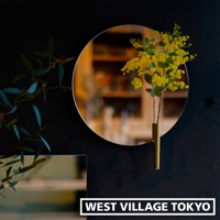 圓形鏡面壁掛花器，黃色小花束置於金色圓柱形花瓶中，與左側的綠色枝葉相互映襯。