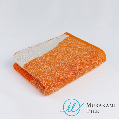 一條橘色與白色相間、質地蓬鬆的毛巾，置於白色背景上，右下角有「Murakami Pile」的品牌標誌。