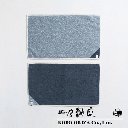 兩條棉麻混紡快乾浴墊，上方為淺藍色，下方為深藍色，皆有白色包邊及角落的品牌標籤。