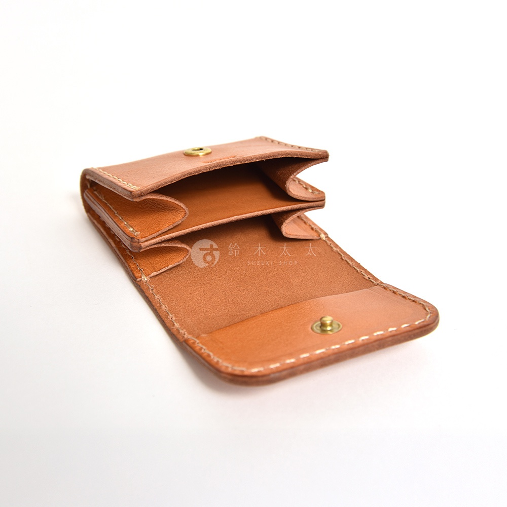 一款棕色植鞣皮革製成的職人手作雙折零錢包，採開放式設計並附有金屬扣環，表面壓印著鈴木太太的品牌標誌，整體呈現簡約質感與細膩縫線工藝，以白色背景呈現出皮革的溫潤光澤。