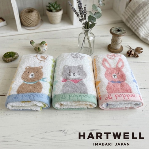 三條並排擺放的 Hartwell 今治森林動物刺繡毛巾，分別繡有棕熊、灰貓與粉紅兔子的圖案，毛巾下方邊緣繡有 poppet 字樣，背景為木質桌面與裝飾小物。