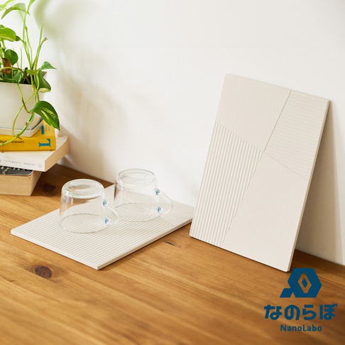 一組兩片淺米色斜面拼接珪藻土瞬間吸水置物墊，其中一片置於木桌上，上面放著兩個玻璃杯，另一片則立於其後，展示其紋理設計。