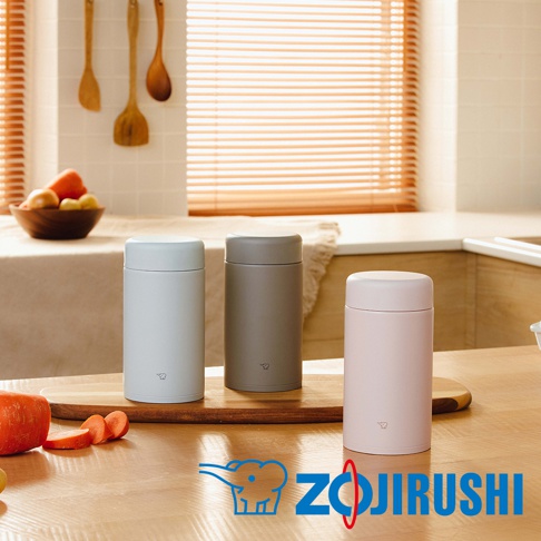 三個不鏽鋼真空燜燒杯，分別為淺灰色、灰色和粉紅色，均配有同色系一體式杯蓋，置於木製砧板上。