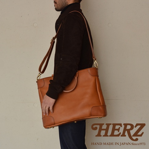 職人手作皮革Organ兩用商務托特包，採用溫潤的棕褐色牛皮製成，包身線條俐落，設有提把及可拆卸的側背帶，適合商務場合使用。