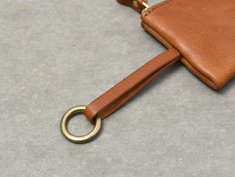 職人手作的棕色皮革鑰匙包，配有黃銅色金屬環和皮革掛繩，展現細緻的縫線與皮革紋理。