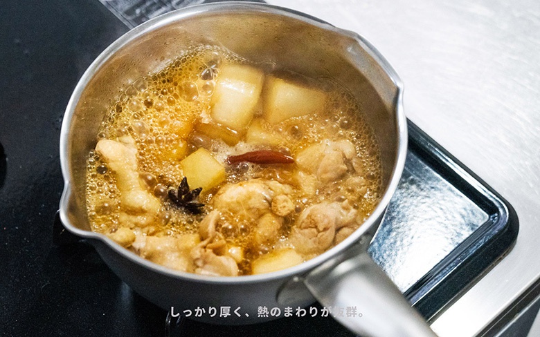 一個銀色不鏽鋼雪平鍋，鍋中煮著雞肉塊、塊狀馬鈴薯、八角和一根辣椒，湯汁冒著泡泡。