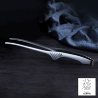 銀色金屬製不沾桌公筷夾/餐夾，一體成形設計，夾頭帶有防滑紋路，握柄處有扇形凹槽，置於深色木紋桌面上，背景為藍色皺褶布料。