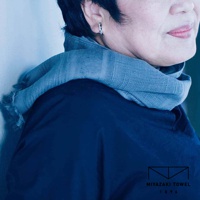 一位女士頸部圍著一條灰藍色、帶有流蘇邊緣的今治匹馬棉圍巾，圍巾表面有細緻的紋理。