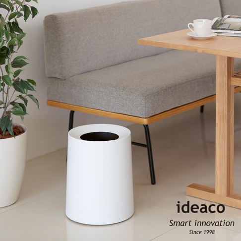 簡約白色圓形家用垃圾桶，上方有黑色開口，置於灰色沙發和木桌旁。
