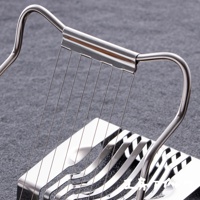 銀色不鏽鋼材質的切蛋器，帶有弧形握把和多條細長的切割線，置於灰色背景上。