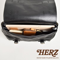 職人手作皮革復古郵差包，黑色，內部可見一個棕色皮夾、一本筆記本和一個平板電腦。