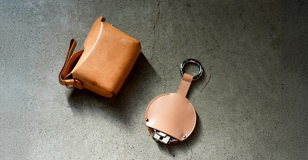 FABRIK 皮革圓形收納鑰匙圈，搭配同材質的方形皮套，置於灰色水泥地面上