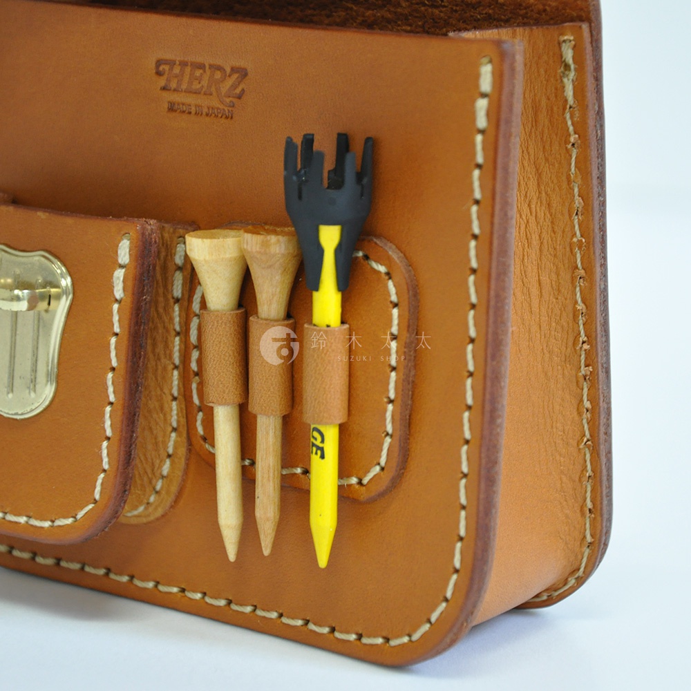 職人手作皮革高爾夫腰包，採用天然皮革材質，呈現溫潤的棕色調。包款設計有置物袋，並插有兩支木質高爾夫球座及一支黃色高爾夫球座。