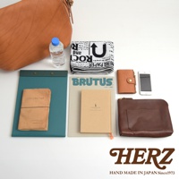 淺棕色皮革郵差包，附有水瓶、毛巾、雜誌、筆記本、小錢包和手機。