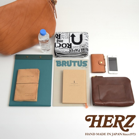 淺棕色皮革郵差包，附有水瓶、毛巾、雜誌、筆記本、小錢包和手機。