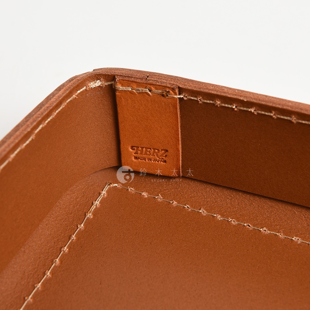 駝色皮革製小物收納盒，盒內有壓印「HERZ MADE IN JAPAN」字樣的皮革標籤，邊緣有縫線裝飾。