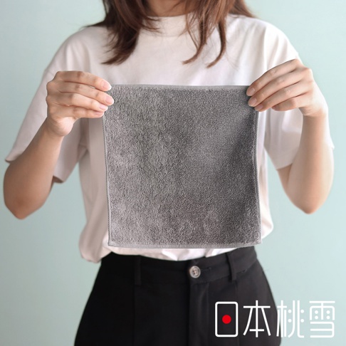 一個女人拿著一塊灰色的毛巾，上面有日文文字「日本桃雪」。