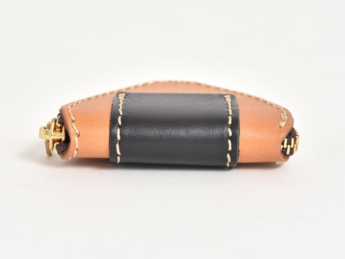 職人手作皮革三角飯糰造型零錢包，採用原色皮革與黑色皮革拼接，搭配金屬拉鍊與米白色縫線，呈現獨特質感。