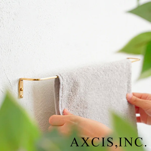 黃銅材質的單桿毛巾架，固定在白色牆面上，一條淺灰色毛巾懸掛其上，被雙手調整。