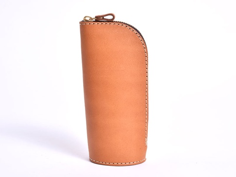 淺棕色皮革製成的直立式筆袋，帶有黃銅色拉鍊和手縫細節。