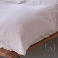 粉色床單特寫，下方可見木質床架，右下角有「W」圖案及 Wasaraf 字樣。