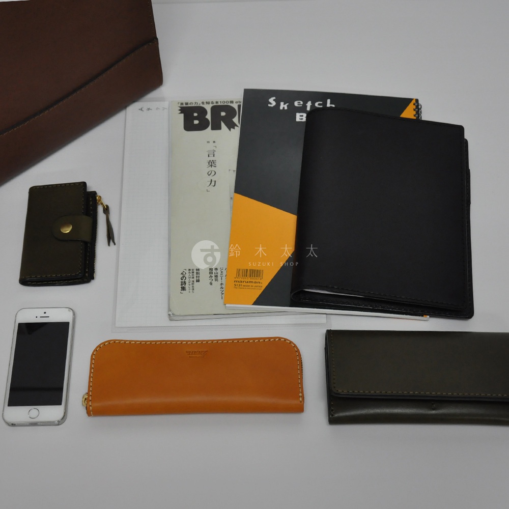 職人手作皮革直式托特包 T-44 M，搭配手機、長夾、筆記本和卡夾，展現皮革質感與收納功能，有多種顏色可供選擇。