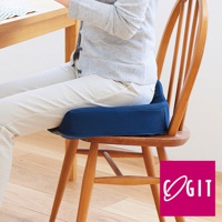 深藍色網狀織物製成的 W 型機能紓壓美尻坐墊，具有特殊弧度設計，置於木質餐椅上，一位身穿灰色毛衣和米白色長褲的人正坐著。