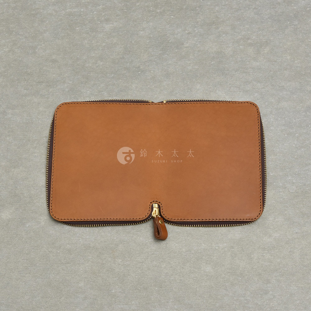 職人手作皮革Organ記事本收納包，設有拉鍊封口和皮革拉環，正面壓印SUZUKI SHOP Logo。