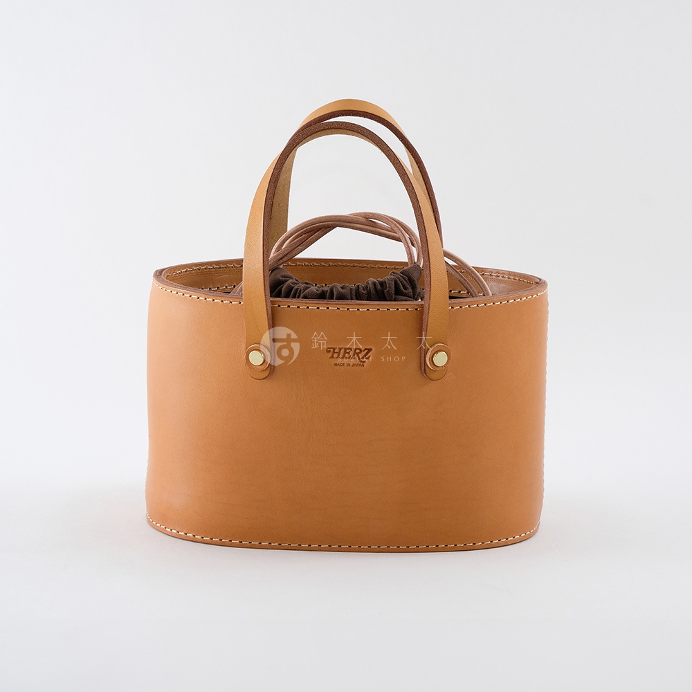 職人手作皮革束口手提包，淺棕色皮革，圓潤桶狀造型，雙提把設計，可見品牌壓印標誌。