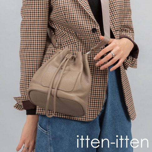 itten-itten 品牌標誌旁，一位女性身穿格紋西裝外套，斜挎一個駝色皮革束口水桶包，牛仔褲搭配。