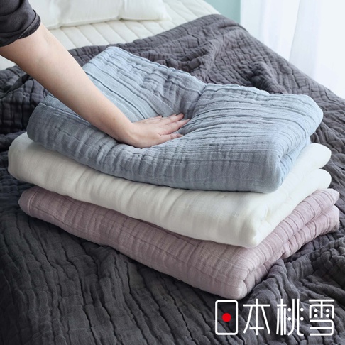 堆疊的八層紗透氣被，顏色由上至下為淺藍、白色、淡紫色，最底層為深灰色。手輕壓在淺藍色被子上，展現其柔軟觸感。